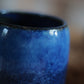 Tumši zilā ombre akmensmasas krūze lietošanā, piepildīta ar kafiju uz galda