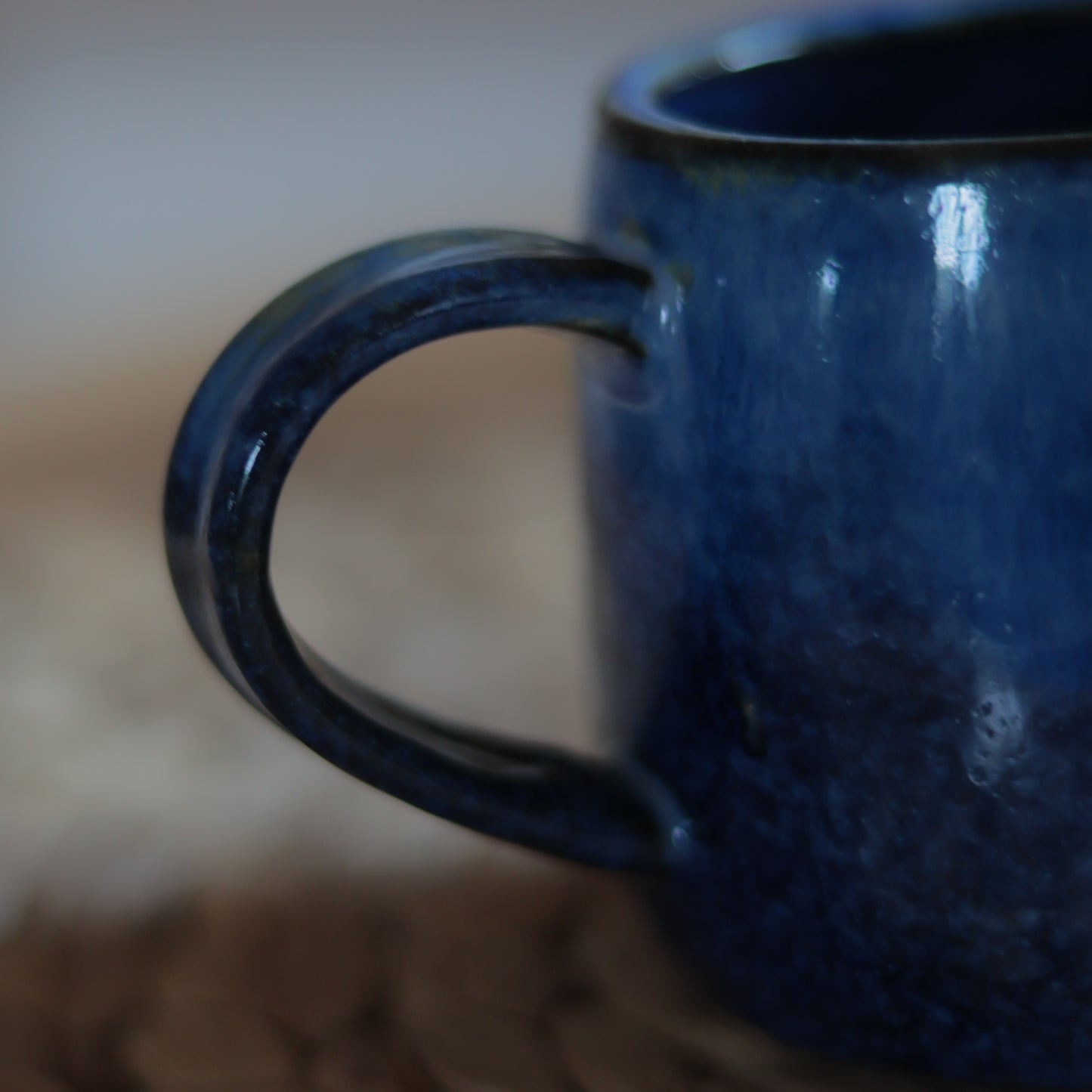 Nahaufnahme des handgeformten Henkels einer blauen Steingut Tasse mit reaktiver Glasurstruktur