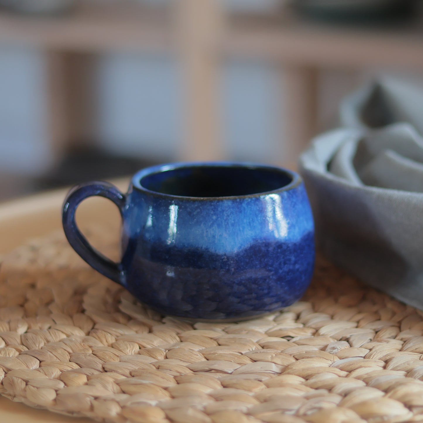 Blaue Steingut Tasse mit Verlaufsglasur und handgeformtem Henkel auf einem Stoffuntersetzer