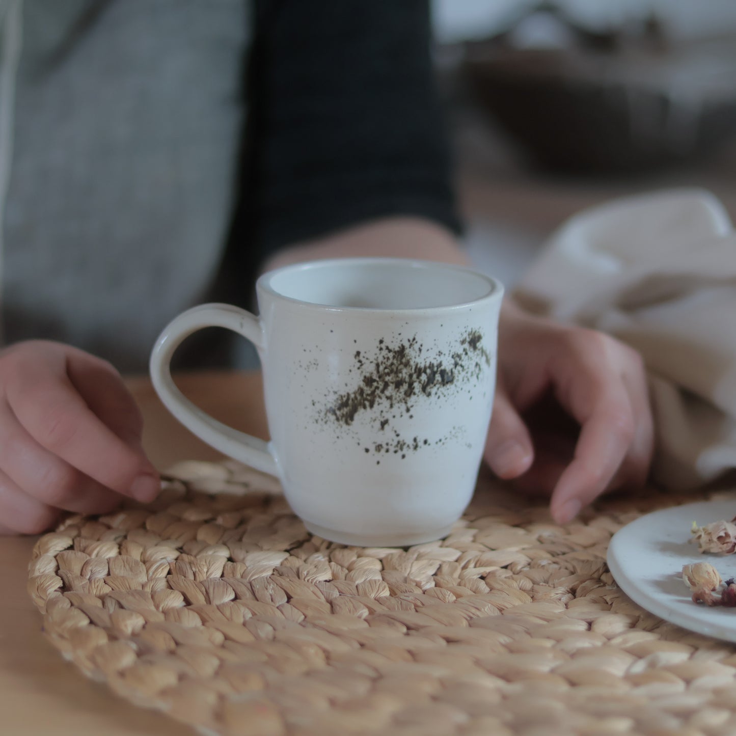 Close-up van een witte gespikkelde stoneware mok met handgemaakt oor op een gevlochten placemat