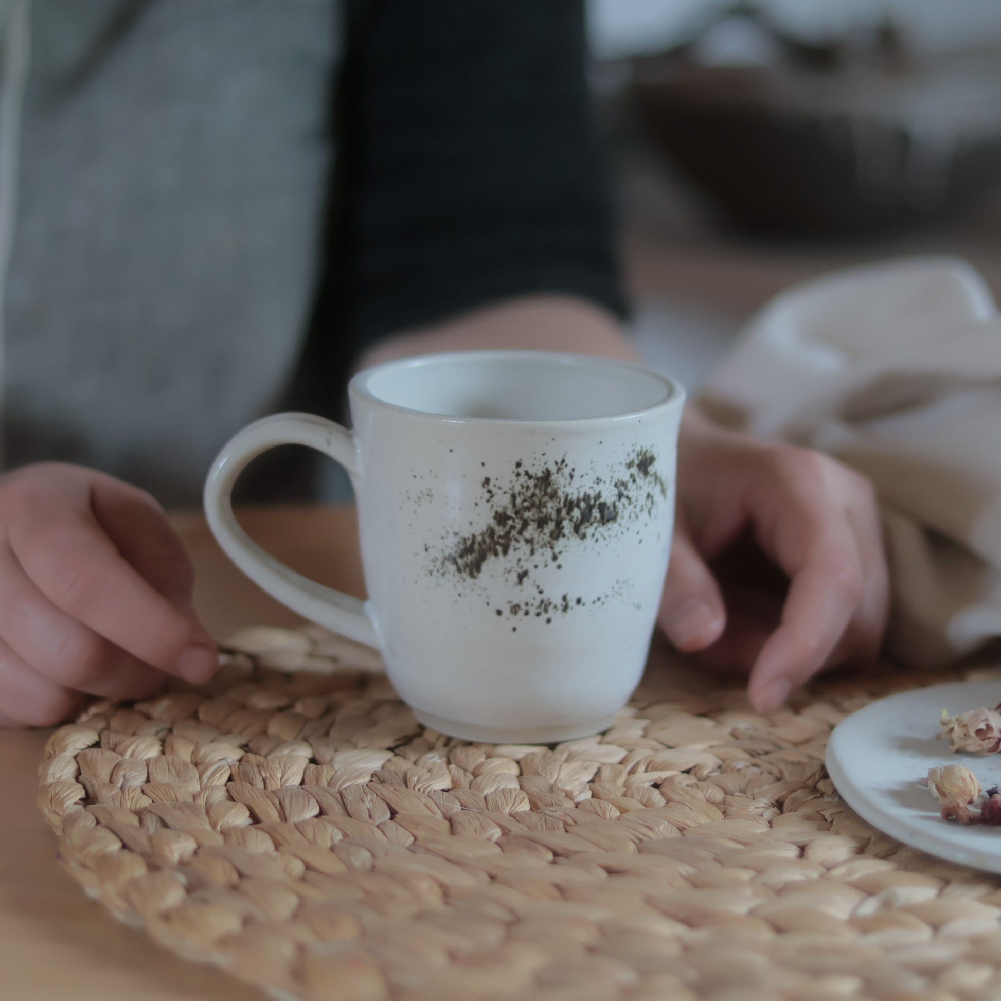 Close-up van een witte gespikkelde stoneware mok met handgemaakt oor op een gevlochten placemat