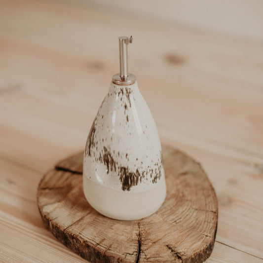 Handcrafted ceramic oil bottle with white speckle glaze and unglazed matte clay body.